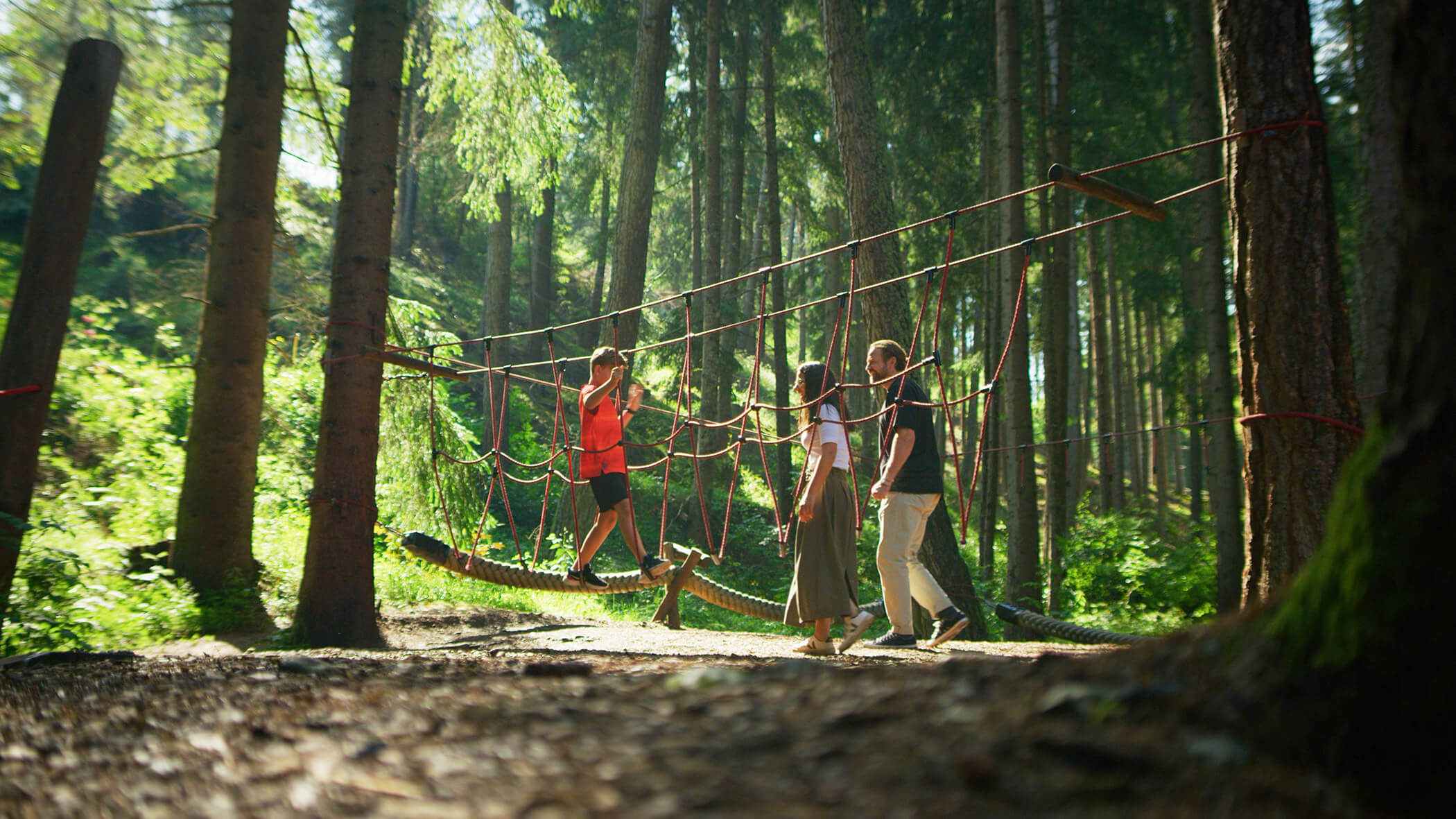Ein Kind im Wald bei einem Kletterparcour und seine Eltern schauen zu - Bad Bergfallerhof